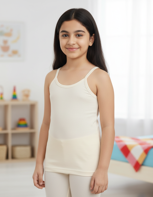 Young girl wearing a white tank top and pants in a room with colorful toys in the background