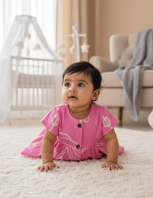 Baby in a pink outfit crawling on a carpeted floor in a nursery.